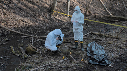 Detectives are collecting evidence in a crime scene. Forensic specialists are making expertise. Police investigation in a forest.