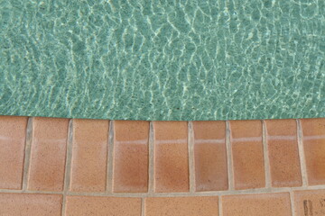 View from above at a swimming pool with green water and tiles edge outdoors. Closeup horizontal...