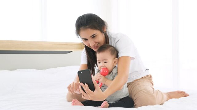 Mother using phone to selfie photo with little baby on bed.