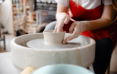Female hands crafting a pottery cup on a potter's wheel. Handmade and crafting concept.