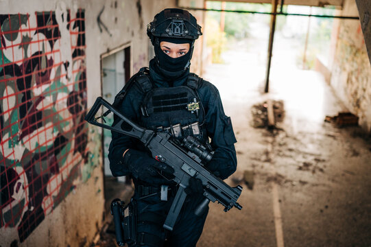 Woman as a police member of swat unit wearing a black jumpsuit and carrying UMP assault rifle. Photos in the abandoned building.