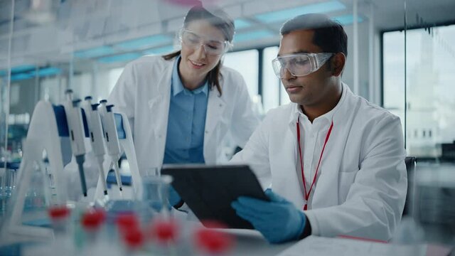 Modern Medical Research Laboratory: Two Scientists Working Together Analyzing Samples, Discussing Innovative Technology