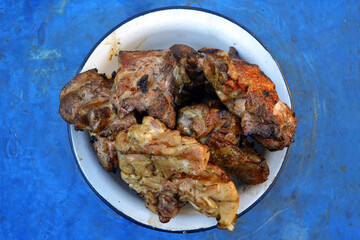 A bowl of roasted meat isolated on the blue background. Close up photo.