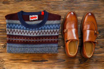 Fototapeta na wymiar Top view shot of folded sweater with festive pattern and brown men's shoes. Set of male clothing. Close up, copy space, flat lay, background.
