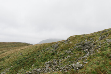 elevated view on mountain hill in lake district england uk during winter with wet foggy hazy cloudy weather rocks and grass