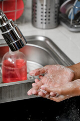 Fototapeta premium Closeup image of Hands being washed using soap under water shower on a kitchen sink to maintain hygiene and healthcare. Healthy lifestyle