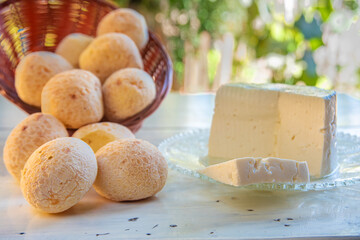 Cheese bread from Brazil, paes de queijo and minas cheese on an old white table with blurred nature in the background, natural light, selective focus.