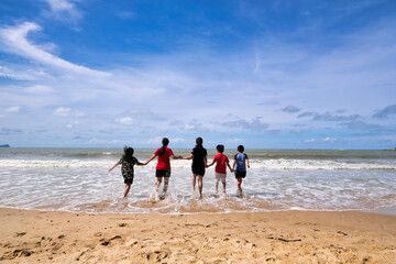 Rear view of family running on the beach towards the sea