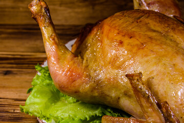 Plate with roasted whole chicken and lettuce leaves on a wooden table