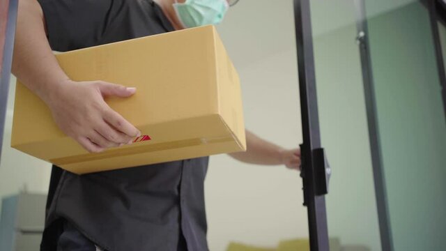 Close up hand Blue delivery man wearing protection mask and medical rubber gloves sending the parcel cardboard to the customer.4K Resolution.
