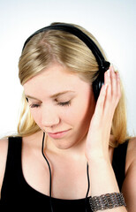 Naklejka premium Blonde girl with headphones. Looking down, holding hand on left ear. Studio photo isolated on light blue background.