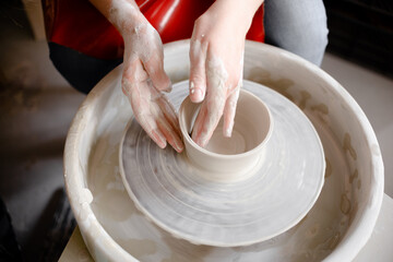 Female hands crafting a pottery cup on a potter's wheel. Handmade and crafting concept.