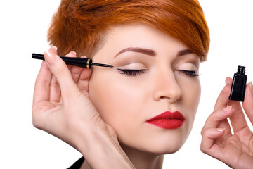 Makeup artist applying black eyeliner close-up. Beautiful young woman with short red hair. Makeup detail.
