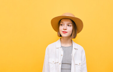 Cute girl in shirt and hat on yellow background, looks aside with serious face, close portrait. Lady in summer clothes is isolated on an orange background, looking at a blank space.
