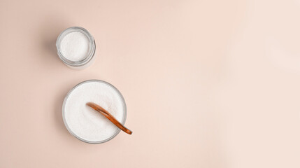 Top view of collagen powder or protein in a glass bowl and small wooden spoon on beige background with copy space. Healthy lifestyle concept.