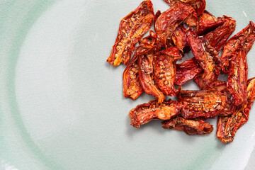 Sun dried tomatoes slices with Italian herbs and spices on mint colored ceramic surface. Homemade dehydrated vegetable.