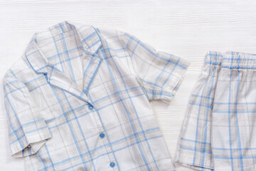 White cotton pajamas with blue checks or stripes, on a white wooden background.  Nightwear for...