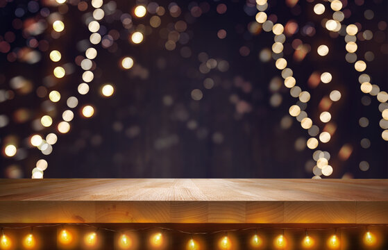 A wood table, tabletop product display with fairy lights under it and a festive Christmas background of hanging fairy lights against a dark backdrop.