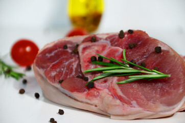 pieces of raw pork steaks, with ingredients for cooking, served on woodenboard. with rosemary, cherry tomatoes, black pepper and olive oil on the table Concept of food preparation on white background