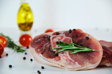 pieces of raw pork steaks, with ingredients for cooking, served on woodenboard. with rosemary, cherry tomatoes, black pepper and olive oil on the table Concept of food preparation on white background