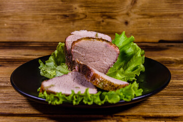 Slices of baked pork meat and lettuce leaves on a black plate