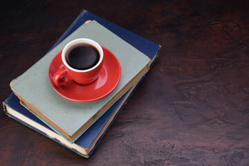 Red coffee cup and saucer with dark black coffee pasted over an old book on a needle colored table - top view with copy space.