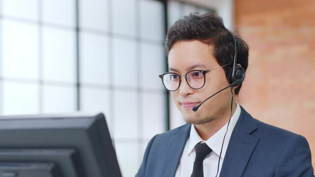 Closeup Asian man call center, customer service, telesales in formal suit wearing headset or headphone talking with customer in modern office