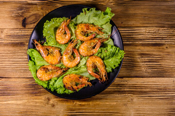Plate with grilled shrimps and lettuce leaves on a wooden table. Top view