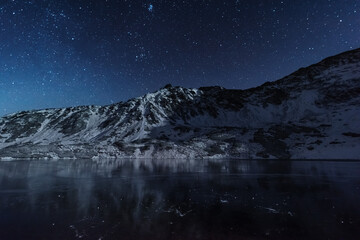 Starry sky in winter Polish Tatras near a mountain lake covered with ice