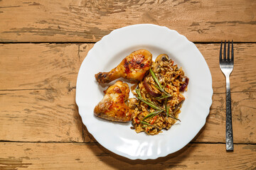 Baked chicken drumsticks and wings marinated with risotto in a plate on the table next to a fork. Copy space