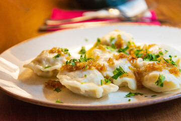 Delicious homemade polish dumplings stuffed with meats and caramelized onions on top served in white plate.