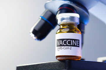 Vial of Covid-19 vaccine next to a microscope