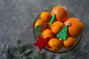 Obraz na płótnie Canvas mockup fruit tangerines in a glass dish with new year decor on a gray background with branches of a christmas tree 