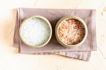 Pink Himalayan rock salt and white mineral salt in a ceramic bowls and spoon on a light background