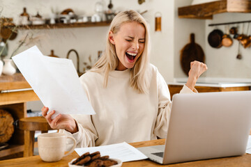 Beautiful excited woman making winner gesture while working with laptop