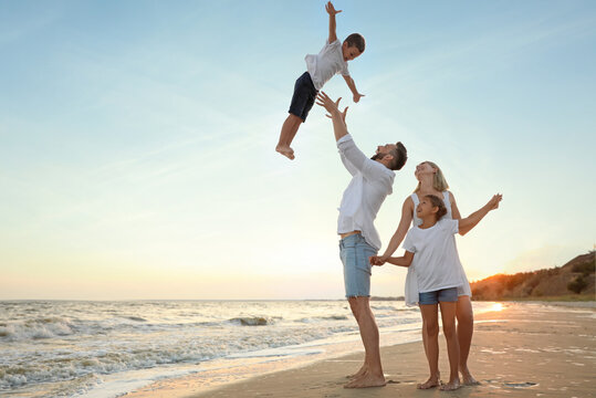Happy family having fun on sandy beach near sea at sunset