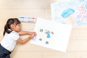 フローリングの床で大きな画用紙に絵を描いて遊ぶ1人の幼い女の子の俯瞰