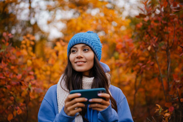 Beautiful happy woman using cellphone while strolling in autumn forest