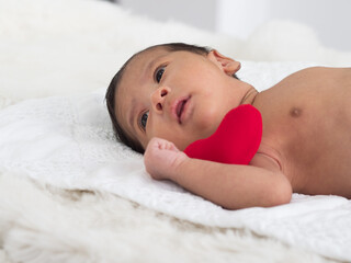 Cute little Asian baby boy lying down with red heart on white blanket.