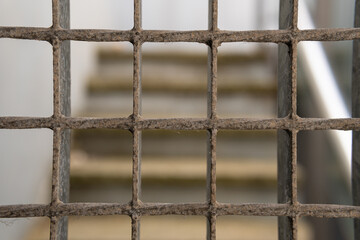 Deteriorated iron fence. At the background of the image an unfocused staircase