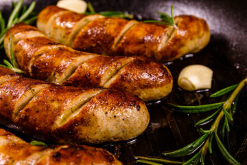 Roasted sausages with rosemary twigs and garlic in a cast iron grill pan