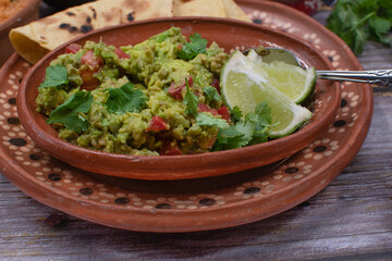 Traditional chunky guacamole with corn tortillas in traditional mexican clay dishes