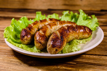 Plate with roasted sausages and lettuce leaves on a wooden table