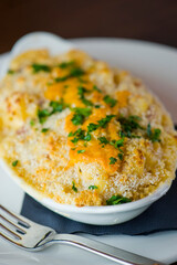 Potatoes au gratin. Potatoes baked in butter, cheese cream sauce, garnished with scallions, parsley and served in cast iron skillet. Classic American restaurant or French bistro side dish.