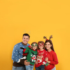 Family in Christmas sweaters and festive accessories on yellow background
