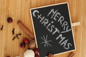 Merry Christmas Hand Drawn Lettering. Wreath of spices, white sweets, black table. Kitchen interior. 