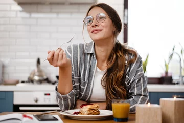 Fotobehang Smiling beautiful woman eating pancakes while having breakfast © Drobot Dean