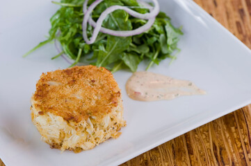 Crab cake. Crab served with spicy rémoulade sauce on top of a mixed green salad. Jumbo crab meat mixed with garlic, onions, spices & fried in butter. Classic American restaurant appetizer.