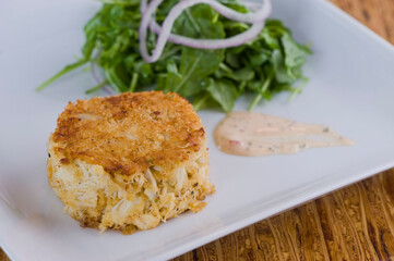 Crab cake. Crab served with spicy rémoulade sauce on top of a mixed green salad. Jumbo crab meat mixed with garlic, onions, spices & fried in butter. Classic American restaurant appetizer.