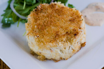 Crab cake. Crab served with spicy rémoulade sauce on top of a mixed green salad. Jumbo crab meat mixed with garlic, onions, spices & fried in butter. Classic American restaurant appetizer.